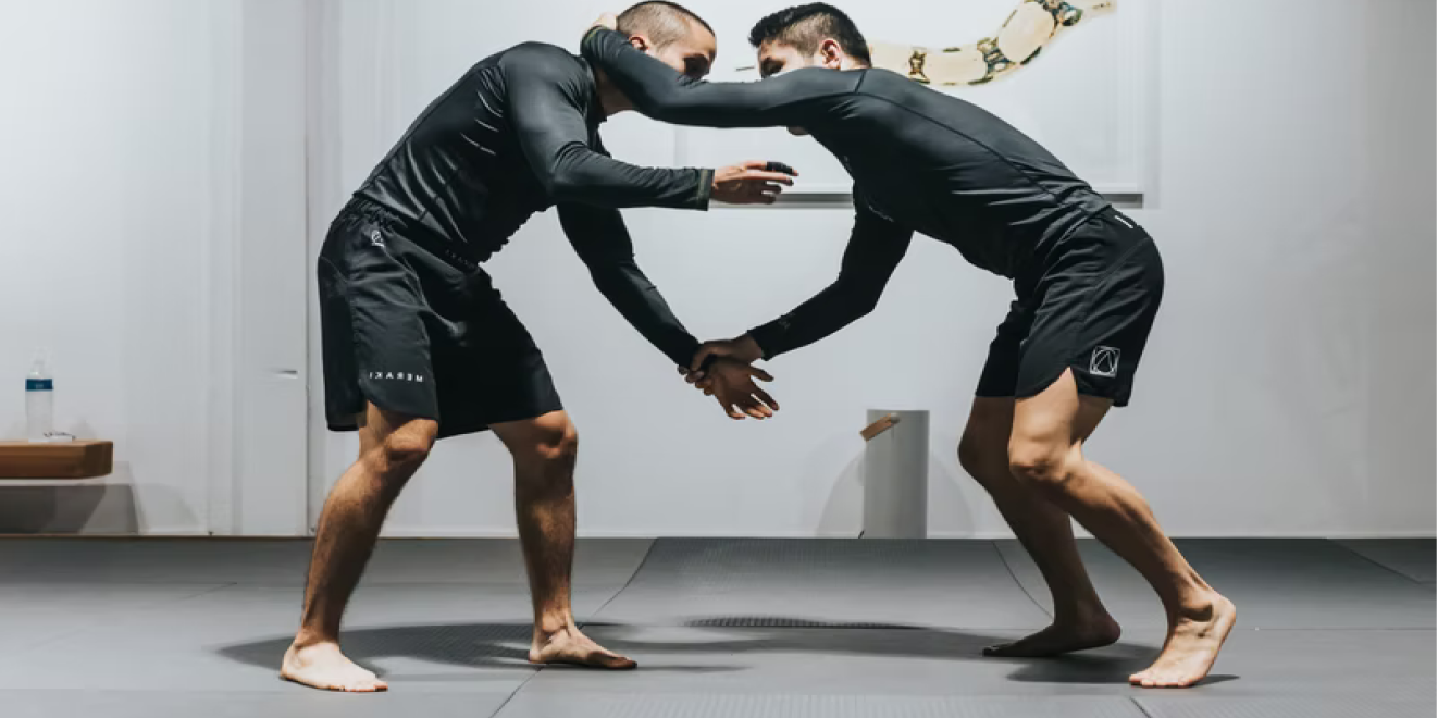 Two grapplers doing no-gi Brazilian jiu-jitsu in a gym